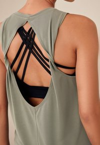 Olivgrünes ärmelloses Top mit einem verdrehten Rückendesign, das schwarze Träger darunter hat. Der Stoff wirkt weich mit einer glatten Textur.
