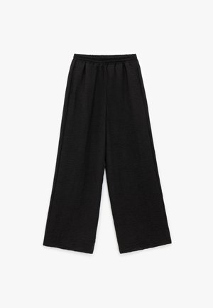 Pantalones negros de pierna ancha con una tela texturizada y una cinturilla elástica. El diseño presenta un ajuste holgado y relajado sin cierres visibles.