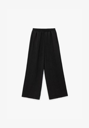 Sorte, brede bukser med en tekstureret stofkvalitet og en elastisk talje. Designet har en løs, afslappet pasform uden synlige lukninger.