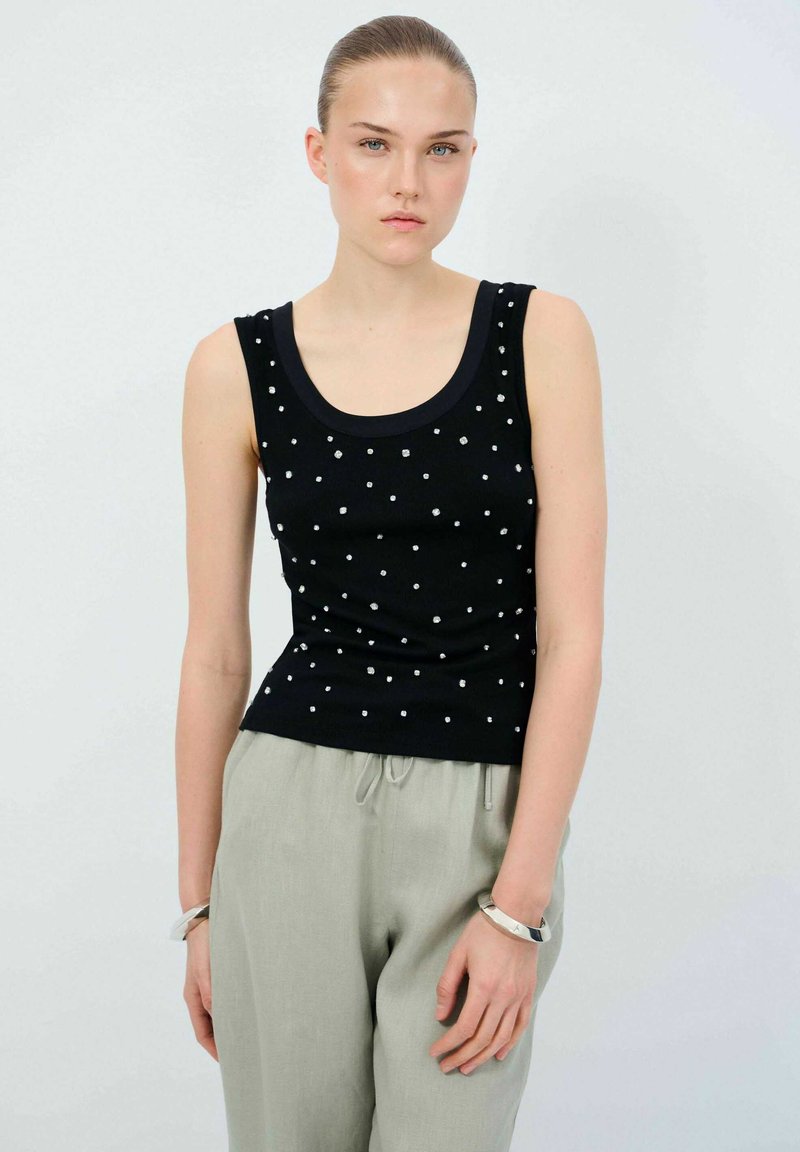 Svart linne med rundad halsringning, dekorerat med silverfärgade fyrkantiga nitar, matchat med ljusgrå linnebyxor. Slät textur och figurnära design.