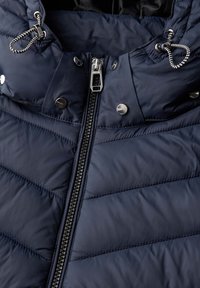 Veste en duvet navy avec un col montant, fermeture éclair argentée et boutons-pression. Présente un motif en chevrons matelassé et un cordon de serrage à la capuche.