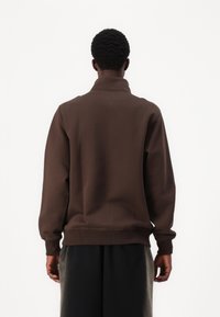 Brun sweatshirt med høj krave, ribmede manchetter og kant. Blød tekstur og afslappet pasform, med minimale syninger.