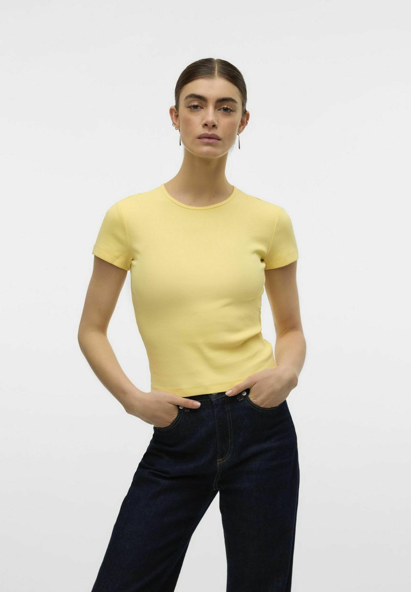 T-shirt gialla a coste con maniche corte e scollatura rotonda, abbinata a jeans in denim scuro. Design semplice, texture liscia.
