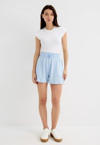 Pantalones cortos azul claro con cintura elástica y cordón, que cuentan con dos bolsillos frontales. Combinados con una camiseta blanca ajustada de manga corta y zapatillas blancas.