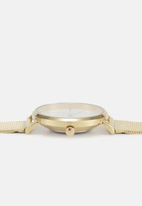 Montre dorée avec un cadran rond, bracelet en maille beige texturé, et un cadran blanc simple. Présente une couronne sur le côté pour le réglage.