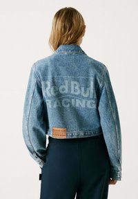 Plava traper jakna s krojenjem iznad struka, velikim ovratnikom, Red Bull Racing logotipom na leđima i smešnim kožnim oznakom blizu donjeg ruba.