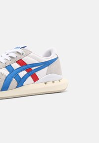 Grey and white sneaker with blue and red accents, made of leather and suede, featuring a textured surface and a cream outsole.