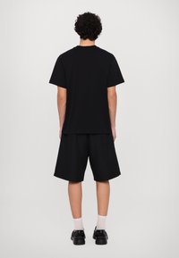 Melna īsām piedurknēm T-krekls un melnas šorti, kokvilnas materiāls, brīvs piegriezums, ar vienkāršu dizainu, apvienots ar melniem apaviem un baltām zeķēm.