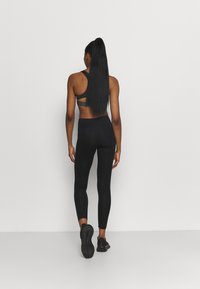 Svart sportbh med cut-out ryggdesign, parat med höga svarta leggings, bärs tillsammans med svarta träningsskor.