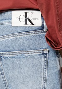Világoskék farmernadrág, látható varrással, egy fehér címkével, amelyen a "Calvin Klein Jeans" felirat olvasható, és egy zseb a hátulján.