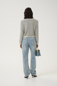 Grå teksturert genser med lange ermer, kombinert med lyseblå høywaist jeans. Holder en liten blå og gul veske.