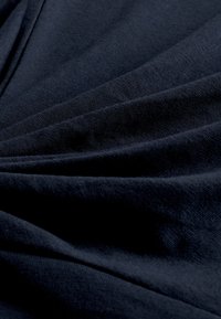 Navy blue fabric with a smooth texture, featuring gently folded layers that create depth and subtle shadowing across the surface.