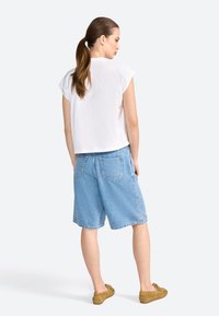 Haut blanc à manches courtes avec une coupe décontractée, associé à un short en denim bleu pâle. La tenue présente des coutures simples et un design décontracté.