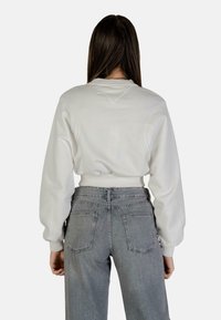 Felpa bianca con maniche lunghe e a sbuffo, orlo a coste, abbinata a jeans grigi chiari a vita alta con tasche posteriori.