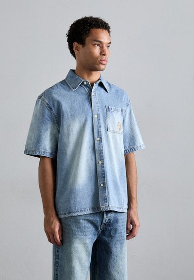 Lichtblauw, korte mouwen denim shirt met een borstzak en knoopsluiting. Verbleekt gradient ontwerp, lichte textuur zichtbaar op de stof.