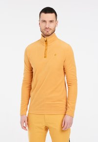 Pullover in pile giallo con colletto alto, zip a quarti e dettaglio del logo. Maniche lunghe e tessuto testurizzato con una finitura liscia.