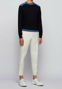 Maglione nero con spalline azzurre, abbinato a pantaloni tapered color crema e scarpe bianche con lacci. Design minimalista, texture liscia.