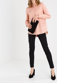 Jasnoróżowa koszula z guzikami, czarne dopasowane spodnie, czarna kopertówka i czarne szpilki. Prosty design, gładki materiał i dopasowany krój.