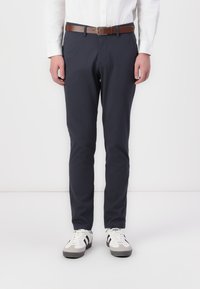Chinos bleu marine en coton, avec une coupe droite, des poches avant, une ceinture en cuir brun, et portés avec des baskets blanches aux accents gris.