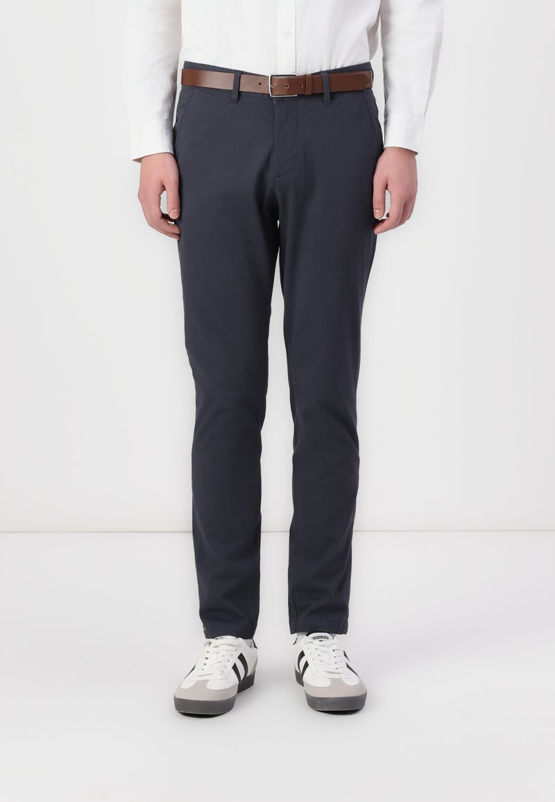 Chinos bleu marine en coton, avec une coupe droite, des poches avant, une ceinture en cuir brun, et portés avec des baskets blanches aux accents gris.