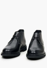 Czarne skórzane botki za kostkę o gładkiej fakturze, zaokrąglonym nosku i sznurowanym fasonie. Grube gumowe podeszwy zapewniają stabilność i przyczepność.