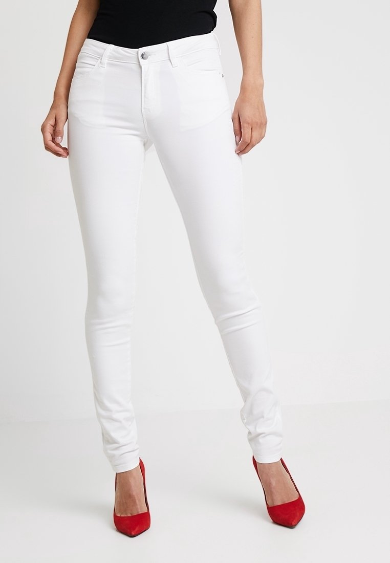 Jean skinny blanc en denim avec une texture lisse, présentant des poches avant et un design classique à cinq poches, accompagnés de talons rouges.