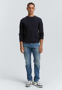 Tamsiai mėlynas ilgomis rankovėmis marškinėliai su apvalia iškirpte, derinami su išblukusiais melsvais džinsais. Batai yra balti su juodais akcentais. Paprastas dizainas, patogus prigludimas.