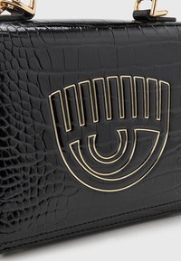 Svart läderväska med krokodilsmönster och emblem i guldton i ögonform på framsidan.