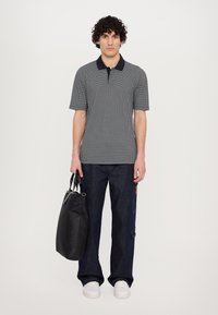 Mørkeblå og hvit mønstrete polo skjorte med krage, sammen med mørk denim bukser. Personen holder en svart tote bag og har på seg hvite joggesko.