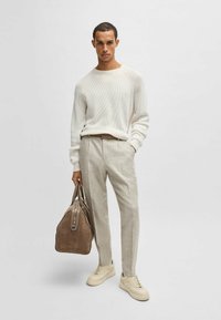 Weißer Strickpullover, beige strukturierte Hose, beige Sneakers und Tasche aus braunem Wildleder. Einfaches, modernes Design mit lässiger Passform und dezenten Akzenten.