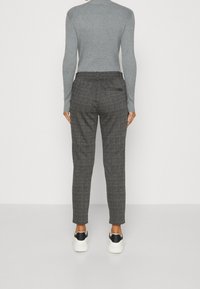 Grijze geribbelde top met lange mouwen, gecombineerd met een donkergrijze geruite broek. De broek heeft een achterzak en is ontworpen met een getailleerde pasvorm.