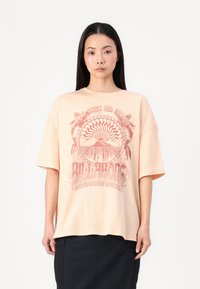  ferskenfarvet oversized t-shirt lavet af bl�ød bomuld. Har et grafisk print med retro-stil tekst og bølgemønstre i rød. Korte ærmer.