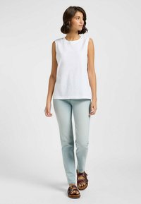 Top blanco sin mangas con escote redondo, combinado con jeans ajustados de color azul claro y sandalias marrones de tiras. Textura de tela suave.