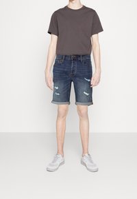 Mörkgrå kortärmad t-shirt i kombination med denimshorts med en slitstark blå finish och uppvikt nederkant. Vita sneakers fulländar outfitten.