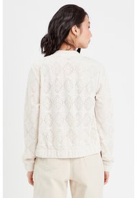 Veste bombardier en dentelle blanc cassé, présentant un design texturé et à motifs avec des poignets et un ourlet côtelés. Vue arrière sans fermetures.