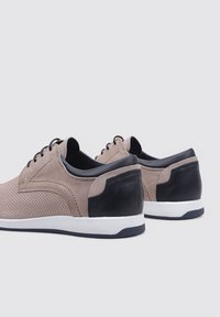 Zapatillas de ante perforado beige con detalles en cuero negro, entresuela blanca y suela de goma negra. Presenta cordones redondos y un cuello acolchado.