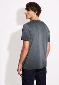 Grå t-shirt med kort ärm och strukturerad yta, rundad halsringning och rak nederkant, tillsammans med mörkblå jeans.