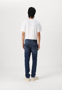 Camiseta blanca de manga corta y jeans de mezclilla azul oscuro, con un ajuste relajado y dos bolsillos traseros, llevados con zapatillas de color claro.