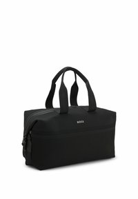 Sac de sport synthétique noir avec deux poignées, fermeture éclair, corps texturé et logo en relief à l'avant. Forme carrée avec un design épuré.