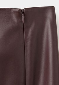Gros plan d'un vêtement en simili cuir brun foncé avec une fermeture éclair centrée dans le dos et une texture de grain visible.