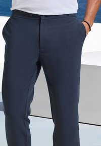 Marineblaue Hose mit glatter Textur, geradem Schnitt und Fronttaschen. Mit Knopfverschluss und leichten Falten an der Taille.
