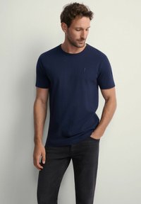Granatowa koszulka bawełniana z okrągłym dekoltem i kr ótkimi rękawami. Z przodu znajduje się małe logo na lewej piersi. Nosi się ją z ciemnymi dżinsami.