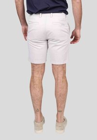 Shorts beige clair avec une coupe ajustée, fabriqués en coton. Ils possèdent deux poches arrière et un léger revers au bas.