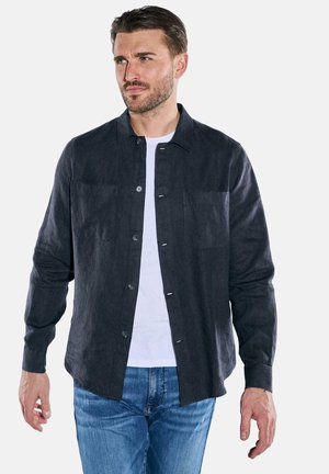 Dark grey linen shirt with a button-up front, two chest pockets, and long sleeves, worn over a white T-shirt and blue jeans.