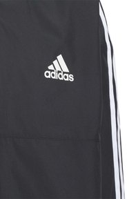 Chaqueta deportiva negra con acentos de tres rayas blancas, que presenta un logo de Adidas blanco bordado en el lado izquierdo del pecho y una textura suave.