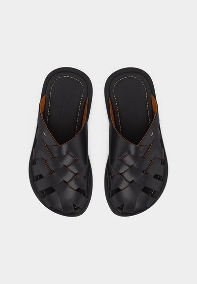 Sandales en cuir noir avec brides tressées, orteils découverts et coutures visibles sur les semelles, vues de dessus sur fond blanc.