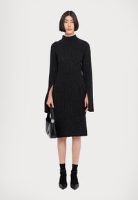 Rochie tricotată neagră cu decolteu înalt, textură ribbed, mâneci lungi, slituri laterale, siluetă ajustată și tiv până la genunchi.