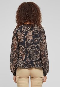 Blusa a maniche lunghe nera con intricati motivi floreali paisley marroni e beige, caratterizzata da una vestibilità comoda e polsini elasticizzati.