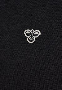 Icône d'abeille brodée blanche centrée sur un fond de tissu noir texturé.