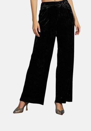 Pantalones de terciopelo negro de pierna ancha con una textura suave y un diseño de cintura alta, que cuentan con una cinturilla plegada y pliegues frontales.